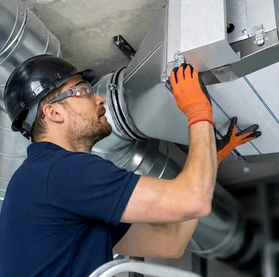 Technician working on heating and ventilation equipment beside metal ductwork