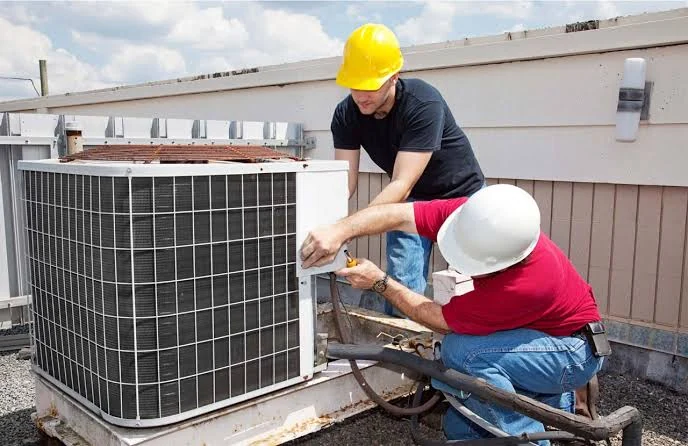 Two HVAC technicians working together on an outdoor air conditioning unit