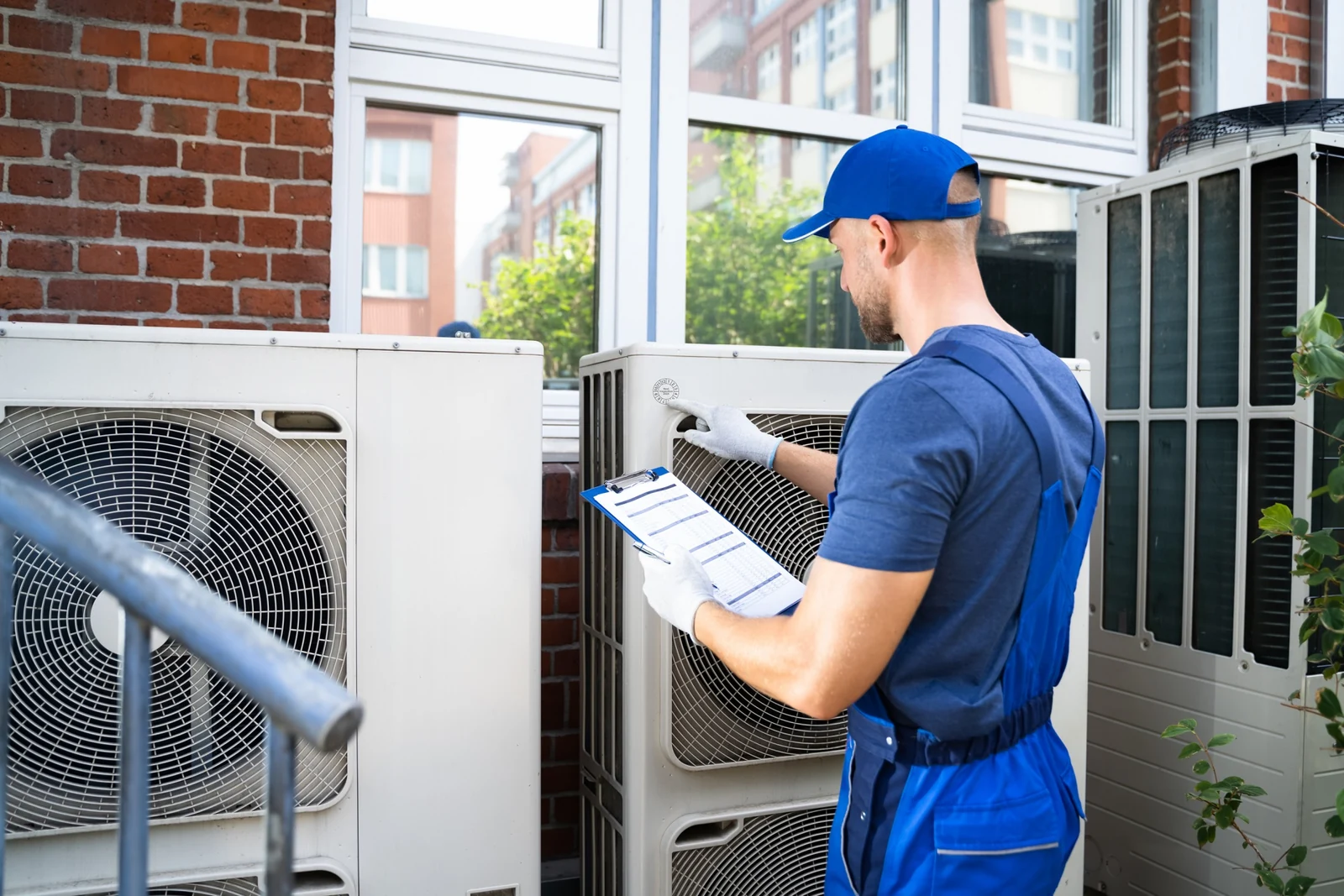 Technician inspecting an outdoor air conditioning cabinet beside a home